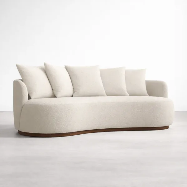 Angled view of ivory boucle curved sofa with cushions and teakwood base by INTERIORZE