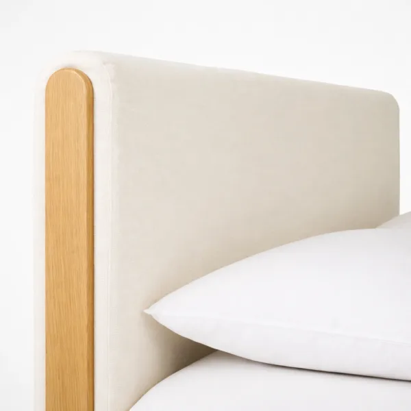 Padded headboard detail of an upholstered teakwood bed with ivory fabric and teak side post