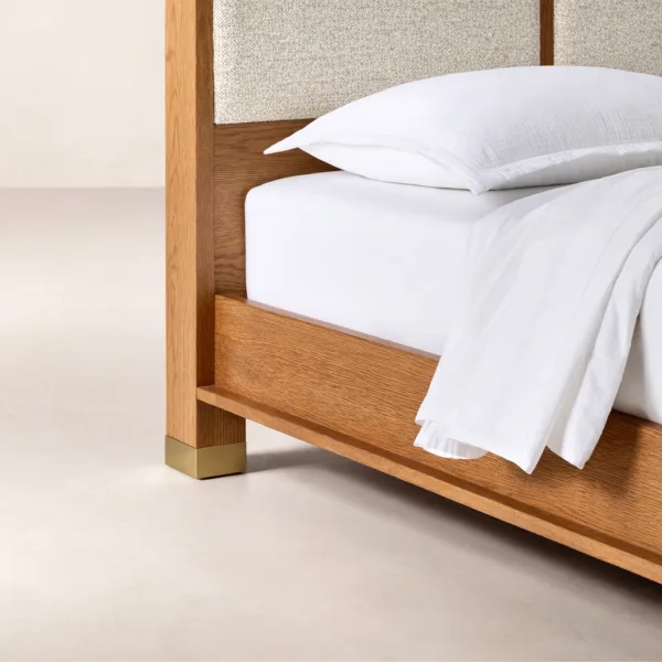 Close-up detail of INTERIORZE Elora teakwood upholstered panel bed showing wood frame, fabric panel, and brass-tone leg cap