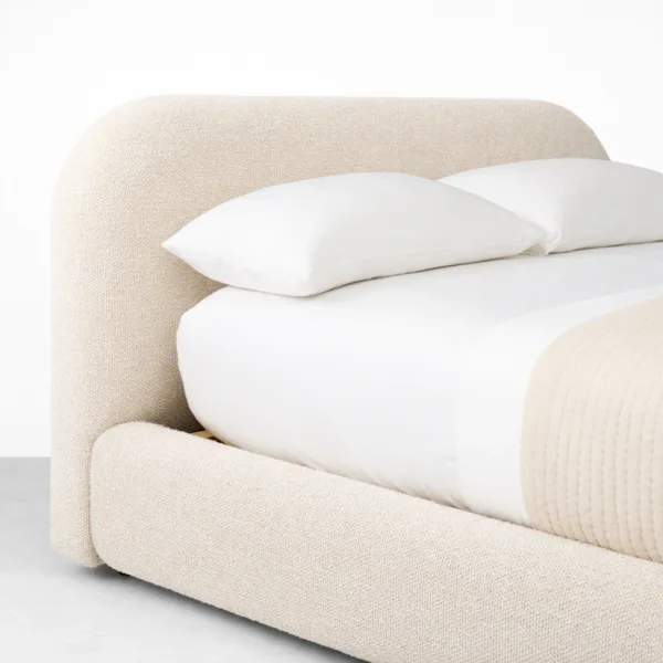 Rounded headboard detail of a fully upholstered bed with textured beige upholstery