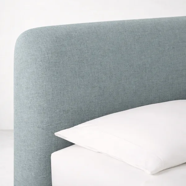 Close-up of curved upholstered headboard on steel blue skirted bed