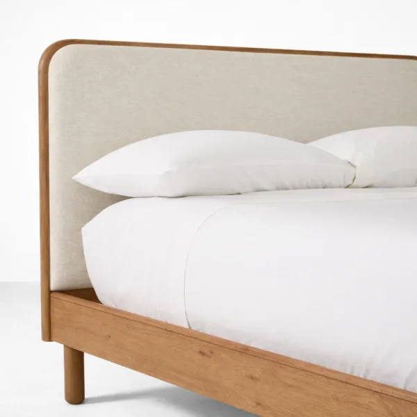 Rounded teakwood frame headboard detail with upholstered fabric panel on an upholstered teakwood bed