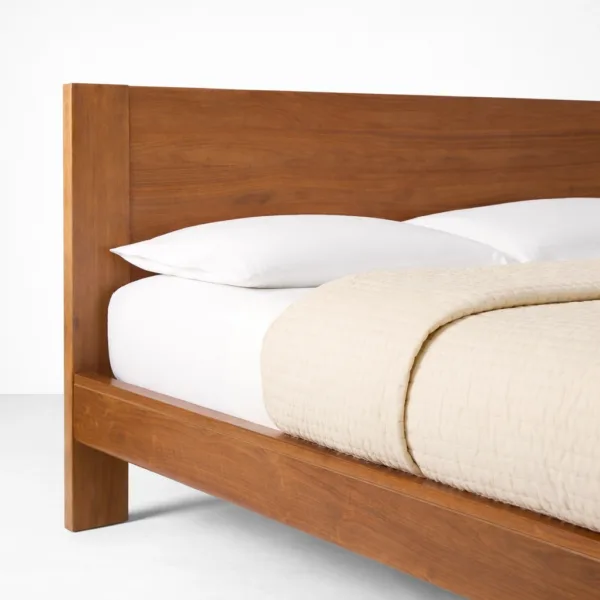Curved panel headboard detail of a solid teakwood bed with visible wood grain finish