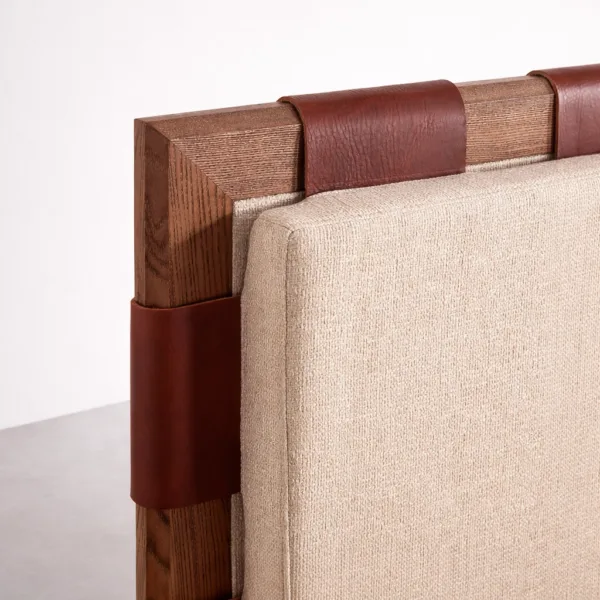 Close-up of teakwood upholstered bed headboard showing leather strap detail and fabric texture
