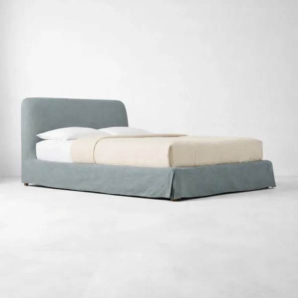 Angled view of steel blue skirted upholstered bed with fabric skirt base