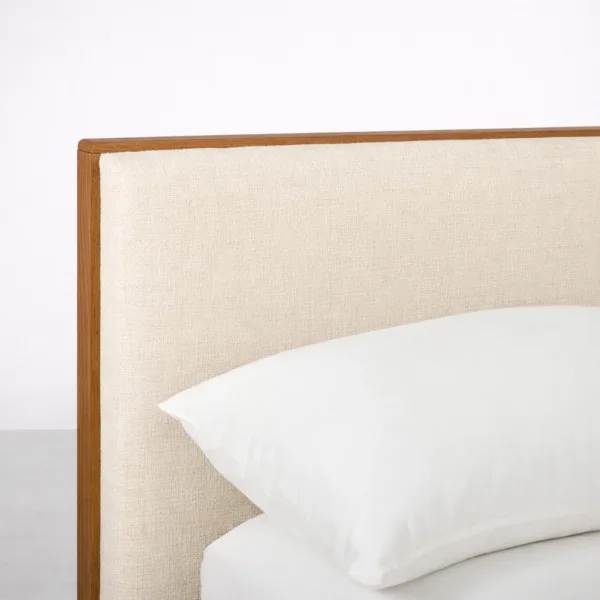 Close-up of beige linen-look upholstery and teakwood trim on bed headboard