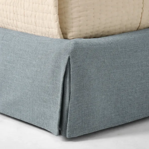 Close-up of tailored fabric skirt on steel blue upholstered bed base