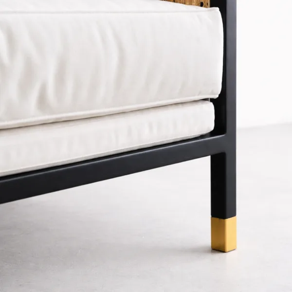 Detail of matte black teak frame and brass toned leg cap on teak cane 2 seater sofa
